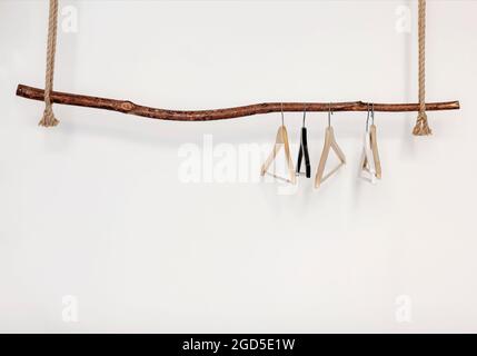 Set aus fünf leeren Kleiderbügeln, die an einer Stange im rustikalen Holzstil an einem dicken Seil hängen, isoliert über einem weißen Hintergrund an der Studiowand mit Kopierfläche für tex Stockfoto