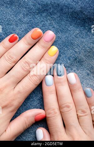 Weibliche Hände mit farbenfroher Maniküre auf Jeans-Hintergrund. Stockfoto