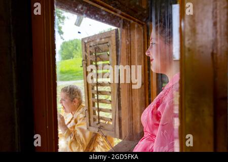 Ivanovo, Vojvodina, Serbien - 17. April 2016: Mädchen in traditioneller Tracht, sie beobachtet die Menschen durch das Fenster. Stockfoto