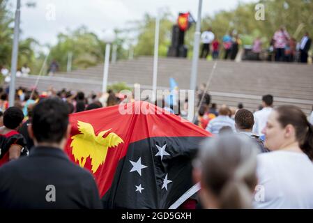 PORT MORESBY, PAPUA-NEUGUINEA - 06. Mai 2018: Nahaufnahme einer Flagge von Papua-Neuguinea, die von jemandem draußen unter vielen Menschen gehalten wird Stockfoto