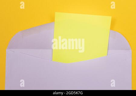 Violette Umschläge mit leerem gelben Blatt Papier innen, auf gelbem Hintergrund liegend - Mock Up with Copy Space. Posteingang oder Benachrichtigung, Postkarte senden - Draufsicht, Flat Lay Stockfoto