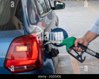 Mann, der sein blaues Auto mit der Hand betankt. Tankwart pumpt Öl in den Vorratstank Stockfoto