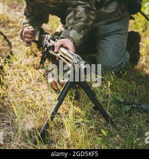 Nicht identifizierter Reenaktor, der als deutscher Soldat mit Maschinengewehrschützer verkleidet ist und mit einem Maschinengewehr auf einen Feind im Wald zielt Stockfoto