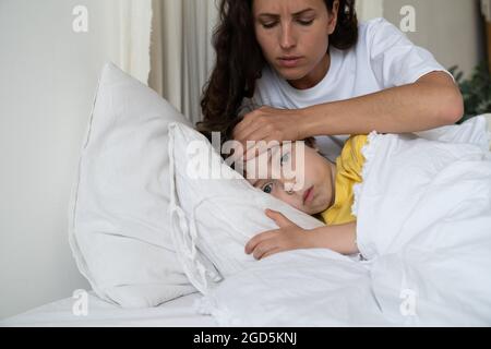 Mutter kümmert sich um kranken Sohn, überprüfen Sie die Temperatur des Kindes berühren Sie die Stirn mit der Hand. Konzept der Kindergesundheitsversorgung Stockfoto