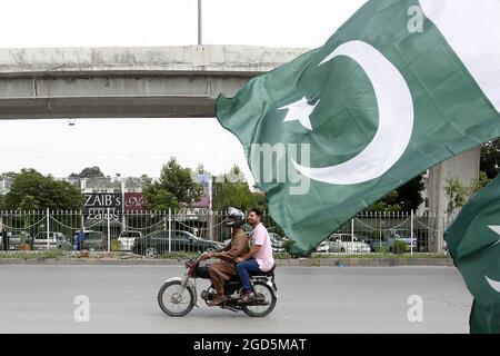 Rawalpindi, Pakistan. August 2021. Ein Motorrad fährt am 11. August 2021 in Rawalpindi, Pakistan, an einer pakistanischen Nationalflagge vorbei. Pakistan wird am 14. August seinen Unabhängigkeitstag feiern. Quelle: Ahmad Kamal/Xinhua/Alamy Live News Stockfoto