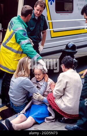 Mitarbeiter von Ambulance Service und umstehende Personen, die nach einem versehentlichen Sturz eine alte Dame auf der Straße besuchten, London, England, Großbritannien Stockfoto