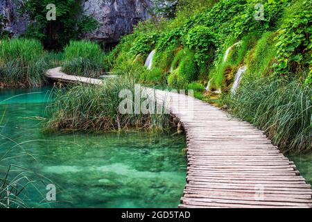 Plitvice, Kroatien - Holzsteg im Nationalpark Plitvicer Seen an einem hellen Sommertag mit kristallklarem türkisfarbenem Wasser, kleinen Wasserfällen und gre Stockfoto