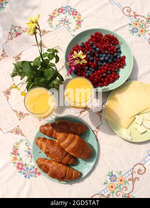 Frühstück auf einem Tisch. Frisch gebackene Croissants, Käse, rote Strömung, blaue Beeren und zwei Gläser Orangensaft. Konzept für gesunde Ernährung Stockfoto