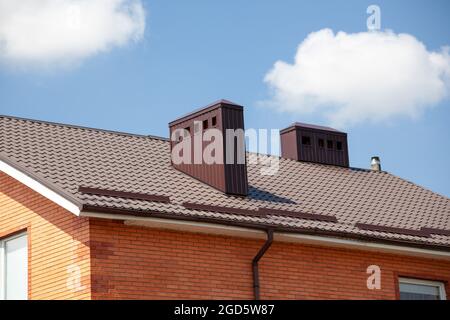 Dachziegel aus rotem Metall und Schornstein. Moderner Kamin auf braunem Dach. Stockfoto