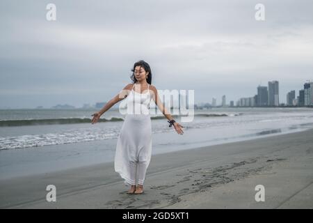 Charmante junge asiatische Frau in weißem Kleid steht mit Händen an der Seite am Strand. Romantisches und friedliches Foto. Hochwertige Fotos Stockfoto