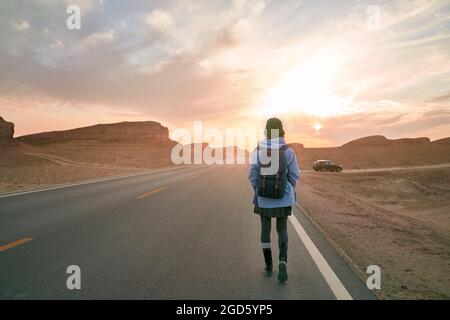 Rückansicht einer Reisenden Frau, die auf der Autobahn in der wüste gobi mit ihren Yardang-Landformen unterwegs ist Stockfoto