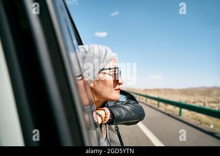 asiatische Frau Touristen, die den Kopf aus der Heckscheibe eines Autos ragt und eine Autoreise genießt Stockfoto