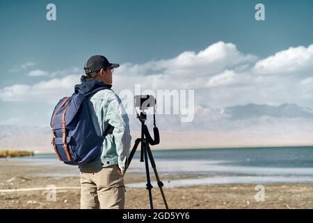 asiatischer Fotograf, der an einem See steht und die Aussicht beobachtet Stockfoto