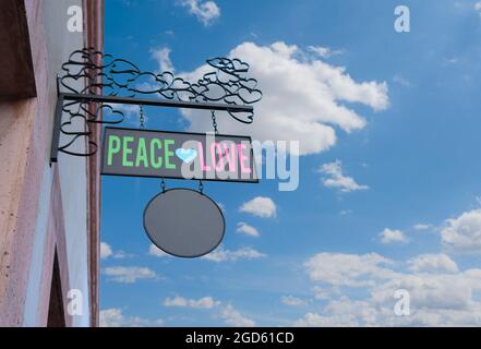 Metallschild mit Phrase der Liebe und des Friedens an der Außenwand eines Hauses mit blauem Himmel und Wolken, ein Herz Stockfoto