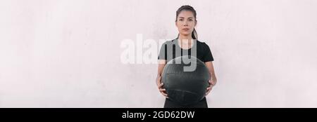 Frau Athlet Cross-Training mit Wurf schweren Medizinball tun Kniebeugen und Ball Slam. Panorama-Banner im Hintergrund des Fitnessstudios. Stockfoto