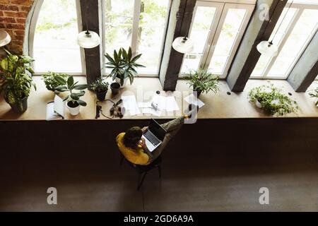 High-Angle-Ansicht des Fotografen, Kameramanns mit professioneller Kamera, Ausrüstung während der Arbeit im Büro, in Innenräumen. Konzept von Beruf, Beruf Stockfoto