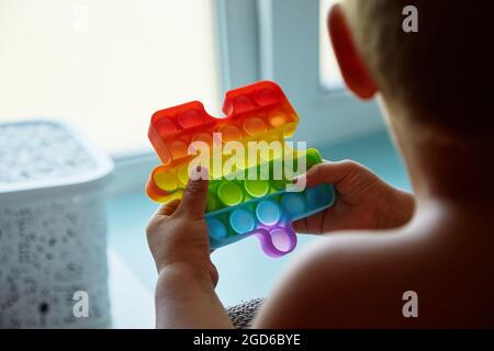 Kleinkind spielt mit Regenbogen Sinnessilikon Spielzeug. Bunte Antistress Sinnesspielzeug Fidget Push Pop es in die Hände des Kindes. Antistress trendy Pop it Spielzeug. Hoch Stockfoto