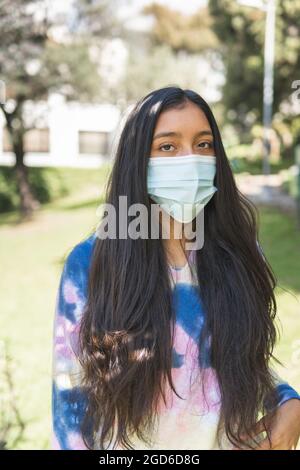 Halblanges Porträt eines brünetten Teenagers mit einer OP-Maske mitten in der Vegetation und Blick auf die Kamera Stockfoto