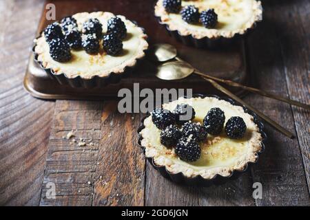Frisch gebackene Minitörtchen mit Brombeeren auf einem Holztisch. Stockfoto