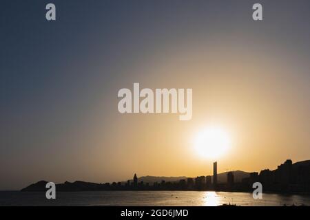 Sonnenuntergang über dem Weststrand in Benidorm, Spanien, mit der Spiegelung der Sonne auf dem Mittelmeer und der Silhouette der Gebäude der Stadt Stockfoto