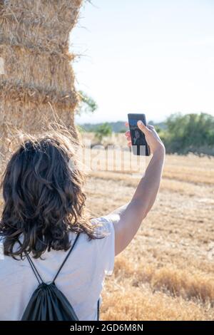 Die brünette Latina-Frau mittleren Alters trägt ein weißes T-Shirt und nimmt ein Selfie vor einigen Strohballen auf. Rückansicht. Speicherplatz kopieren Stockfoto