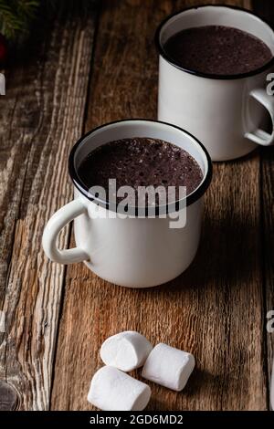 Heißer Kakao in weißen Bechern mit süßem Marschwalben mit Dampf aus der Tasse auf rustikalem Holztisch, Weihnachtsfeiertag Stockfoto