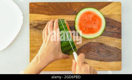 Frau, die Wassermelone auf einem hölzernen Cuttin-Brett aufschlitzt, Nahaufnahme von oben Stockfoto