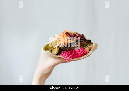Nahaufnahme einer Hand, die vegetarisches Shawarma mit roten Bohnen hält, und Gurken, die in Pita-Brot eingewickelt sind Stockfoto