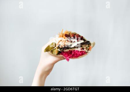 Nahaufnahme einer Hand, die vegetarisches Shawarma mit roten Bohnen hält, und Gurken, die in Pita-Brot eingewickelt sind Stockfoto