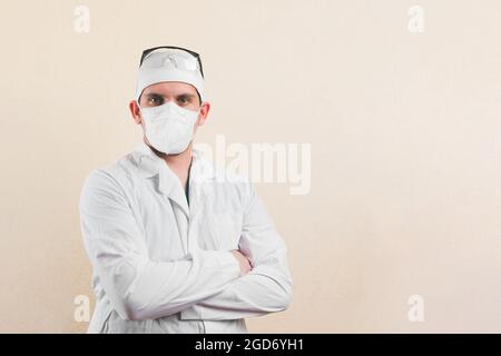 Junger Arzt in wshite Laborkittel, Schutzbrille und schützender Atemmaske mit den Händen auf der Brust auf dem gelben Hintergrund. Stockfoto