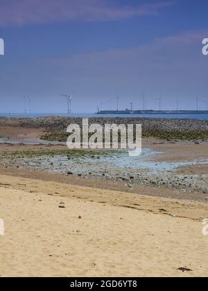 Die Südseite des Gare, die bei Ebbe über den Nordstrand des Gare gesehen wird, mit einem küstennahen Nordsee-Windpark am Horizont unter sich verfestigender Wolke. Stockfoto