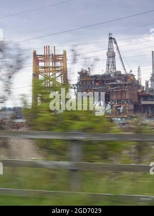 Eine Offshore-Plattform, die stillgelegt wird - aufgenommen von einem fahrenden Auto, macht die Bewegung die Bäume zerbrechlich und vergänglich, im Gegensatz zur Rig. Stockfoto