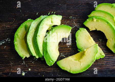 Geschälte und geschnittene Haas Avocado auf dunklem Holzhintergrund: Haas Avocado-Scheiben auf einem Holzschneidebrett Stockfoto