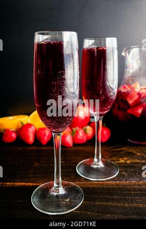 Rotwein-Champagner-Sangria in Flötengläsern serviert: Getränke aus Rotwein, Sekt und frischem Obst, serviert in Weingläsern Stockfoto