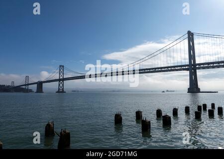 Bay Bridge San Francisco Kalifornien. Hinterleuchtete Brücke mit Resten eines Ponton im Vordergrund Stockfoto