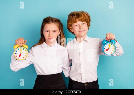 Porträt von zwei attraktiven Freunden halten kindische Uhr umarmt Minute isoliert über hellen blauen Hintergrund. Stockfoto