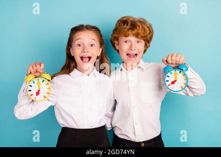 Porträt von zwei attraktiven erstaunt fröhlich Freunde halten kindische Uhr umarmt isoliert über hellen blauen Hintergrund. Stockfoto