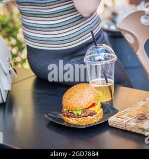 Frischer Burger, Plastikglas Bier auf der Bank und neben der Frau sitzen. Fast Food. Street Food Stockfoto