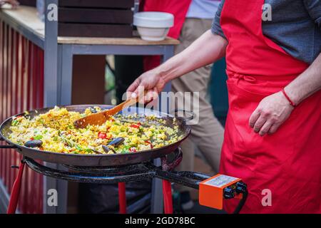 Abstract Kochen Sie in roter Schürze und bereiten Sie Paella im Freien zu. Picknick, Fest, Sommerkonzept Stockfoto