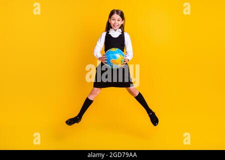 In voller Länge Körpergröße Foto kleine Schülerin springen bis halten Globus in der Schule isoliert lebendige gelbe Farbe Hintergrund Stockfoto