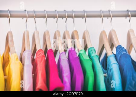 Kleidung hängt an Kleiderständer Kleiderschrank Mode Kleidung Auswahl von Regenbogenfarben T-Shirts auf Kleiderbügel. Damen tragen im Frühjahr im Geschäft einkaufen Stockfoto