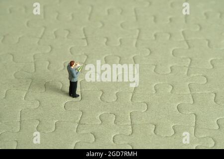 Miniatur Menschen Spielzeug Figur Fotografie. Ein Student der Männer steht über einem unvollständigen Puzzle-Puzzle. Bildfoto Stockfoto