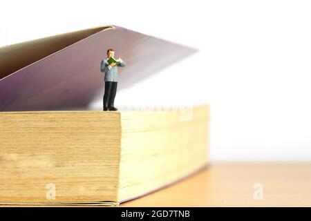 Miniatur Menschen Spielzeug Figur Fotografie. Ein Mann, der über dem Buch stand, öffnete beim Lesen das Buch. Bildfoto Stockfoto