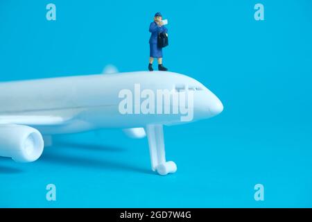 Miniatur Menschen Spielzeug konzeptuelle Fotografie. Paketversand im Flugzeug. Postboten-Kurier mit weißem Flugzeug, isoliert auf blauem Hintergrund. Stockfoto