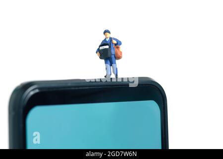 Miniatur Menschen Spielzeug konzeptuelle Fotografie. Mobile Post-Service-Bereitstellung. Postbote, der über dem Smartphone steht, isoliert auf weißem Hintergrund. Stockfoto