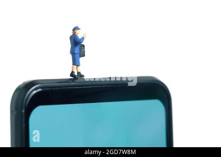 Miniatur Menschen Spielzeug konzeptuelle Fotografie. Mobile Post-Service-Bereitstellung. Postbote, der über dem Smartphone steht, isoliert auf weißem Hintergrund. Stockfoto