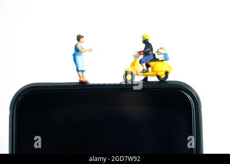 Miniatur Menschen Spielzeug konzeptuelle Fotografie. Mobile Post-Service-Bereitstellung. Postbote, der über dem Smartphone steht, isoliert auf weißem Hintergrund. Stockfoto