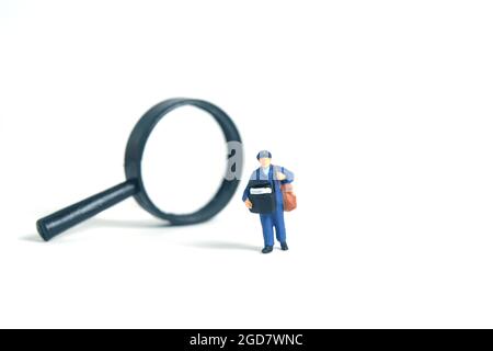 Miniatur Menschen Spielzeug konzeptuelle Fotografie. Adressposition wird gesucht. Postboten-Kurier mit Lupe, isoliert auf weißem Hintergrund. Stockfoto