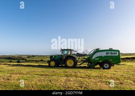 Timoleague, West Cork, Irland. August 2021. An einem warmen und sonnigen Tag stellt Eoin Nyhan von Anthony & Finbar O'Donovan Silage Contractors Ballen auf dem Milchviehbetrieb von Michael Burke mit einem John Deere Traktor 6155R und der Ballenpresse Fusion 3 Plus her. Die Silageballen werden als Winterfutter für Michaels Herde von 250 Kühen verwendet. Quelle: AG News/Alamy Live News Stockfoto