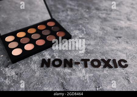 Low tox und natürliche Beauty-Produkte konzeptuelles Bild, Make-up-Palette mit ungiftigem Text auf grauem Hintergrund Stockfoto